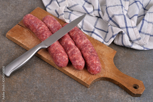 Saucisses de Toulouse crues sur une planche à découper en bois avec un couteau en gros plan sur fond gris