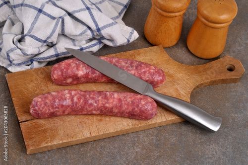 Saucisses de Toulouse crues sur une planche à découper en bois avec un couteau en gros plan à côté d'une salière et d'une poivrière