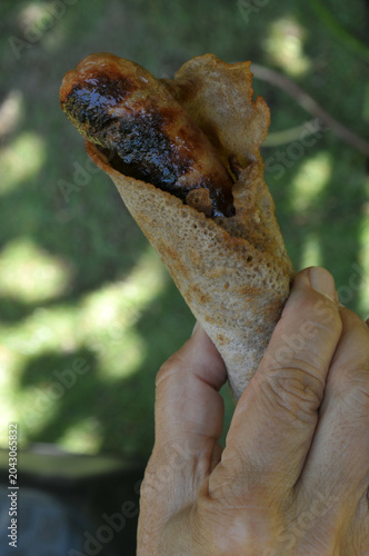 Galette-saucisse bretonne grillée tenue en main en gros plan
