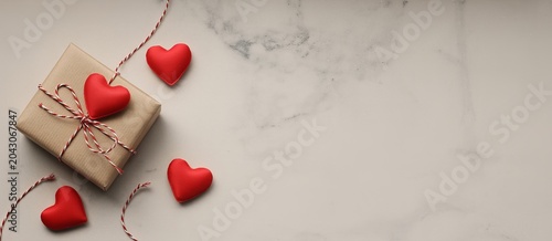 Flat lay of a brown gift box with red ribbon and heart shaped confetti on white surface red hearts