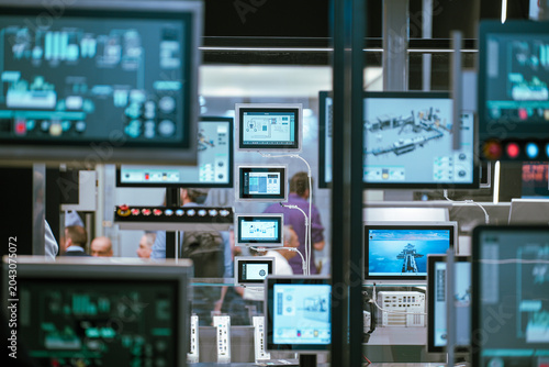 Multiple industrial control panel screens and human-machine interface (HMI) displays show monitoring software data during an automation technology trade exhibition.