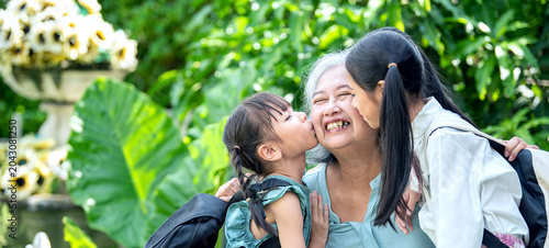 Two granddaughter saying goodbye and kissing grandmother cheek before going to school emotion love family bonding moment. Senior woman receiving kiss from grandchildren in garden at home.