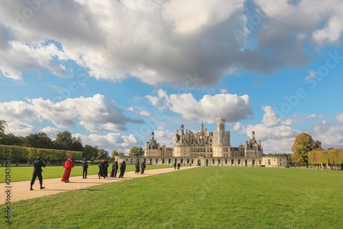 Quadro su tela Visitors dressed in chic attire meander along a winding path surrounded by green