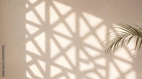 Sunlit geometric lattice shadows on a neutral beige wall with a palm frond accent, creating a warm tropical interior mood