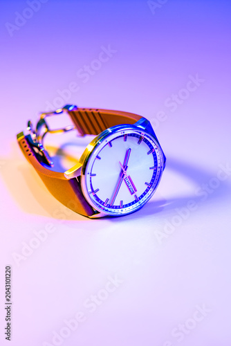 Conceptual Series : A luxury automatic analog wristwatch glows elegantly under vibrant neon blue and magenta lighting.