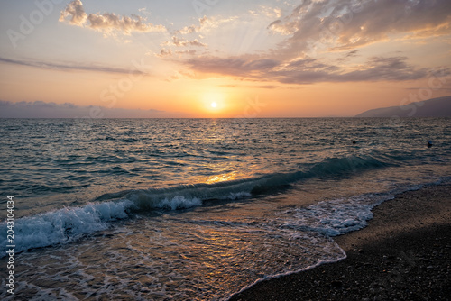 Golden sun sets over ocean waves on a quiet beach in the evening, creating a warm glow on the water as day turns to night