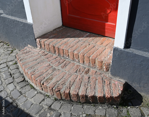 Steps lead to a bright red door at a building on a sunny day in a city setting