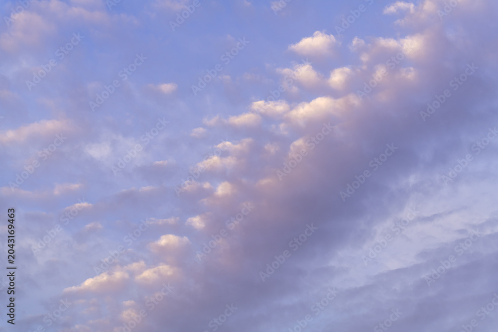Fototapeta premium A beautiful sky with clouds that are white, purple and pink tinted at sunset against a blue sky. 