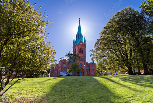Historic Red Brick Church With Copper Spire and Sunlit Park Trees on a Bright Day, Gothenburg, Sweden