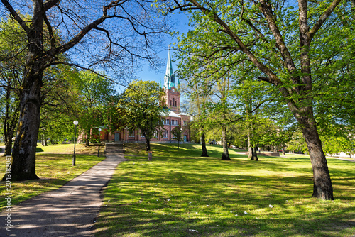 Historic Red Brick Church With Copper Spire and Sunlit Park Trees on a Bright Day, Gothenburg, Sweden