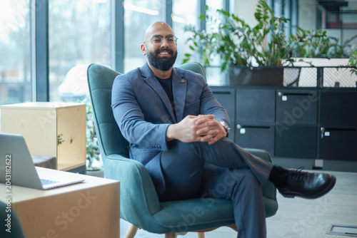 A man in a suit is sitting in a chair in front of a laptop