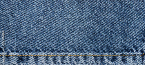 Valokuva Blue denim fabric texture with seam, classic jeans cloth background with yellow stitching and frayed edge