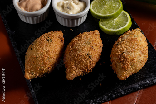 Foto Fried Brazilian Bolinho Croquettes on Slate Platter with Dipping Sauces and Lime