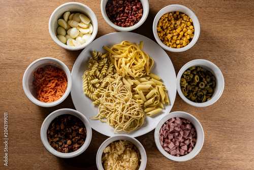Foto Flat Lay of Assorted Pasta Types and Colorful Toppings in Ceramic Bowls on Wood