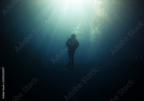Εκτύπωση καμβά Scuba diver silhouette ascending toward dramatic sunburst in deep blue ocean