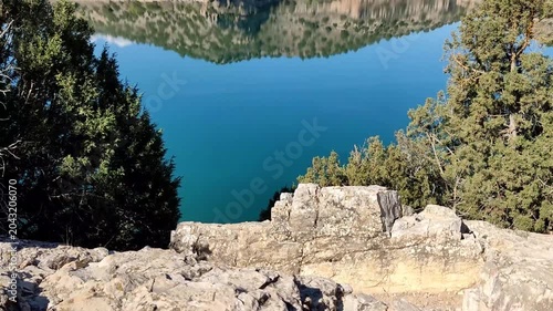 Tilt up view of Arquillo de San Blas reservoir with calm blue water reflecting rocky hills in Teruel Spain