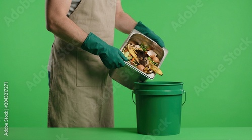 Person wearing gloves disposing food scraps into a green compost bin against a bright green background