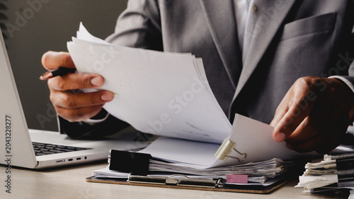 Tableau sur toile Businessman reviews documents near laptop