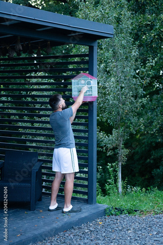 Man placing a birdcage on a patio. Relaxing outdoor scene.