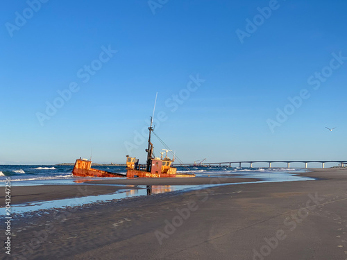 Obraz na plátně Abandoned shipwreck on a wide sandy beach in the Outer Banks of North Carolina, with ocean waves, distant bridge, and expansive blue sky