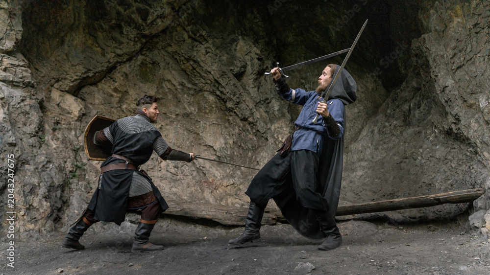 Fototapeta premium Two warriors clash swords amidst a rocky, cavernous setting.