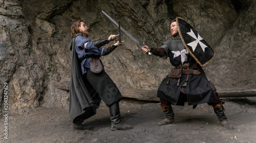 Obraz na płótnie Two warriors clash swords amidst a rocky landscape, embodying medieval combat and fantasy adventure