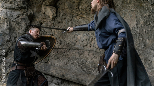 Fotografie Two warriors clash amidst a rocky landscape, their swords poised for battle