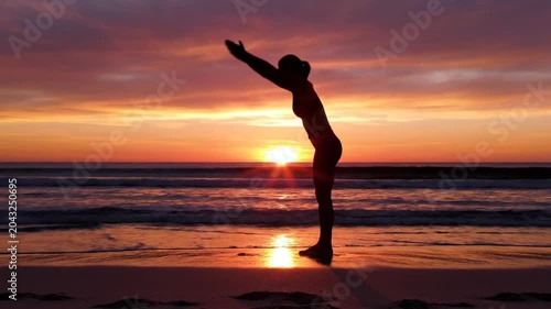 Woman balances in yoga pose silhouette on beach at sunset