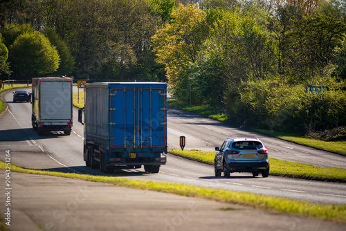 Rear View of a Dump Truck Driving on a Country Road Near Passing Car in Spring Day in England UK
