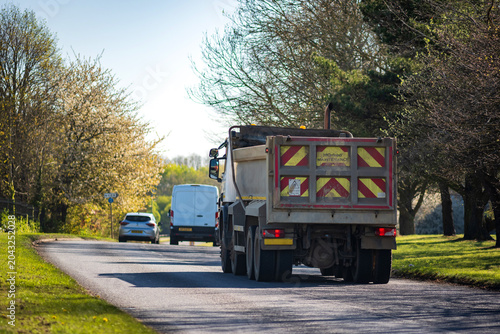 Rear View of a Dump Truck Driving on a Country Road Near Passing Car in Spring Day in England UK