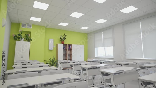 Grid ceiling with square LED panels fills empty room with crisp illumination. Large windows with blinds provide additional soft daylight