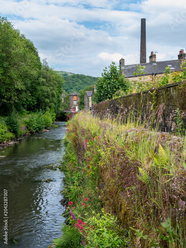 scenic view of a pathway along the river calder in hebden bridge surrounded by summer wildflowers and trees with an old mill chimney and houses