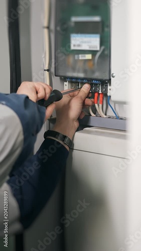 Vertical close up of electrician connecting wiring and servicing electrical control cabinet during industrial maintenance and installation work