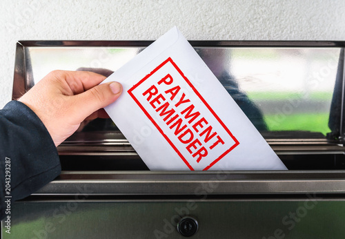 Overdue bills concept: Hand putting payment reminder envelope in mailbox