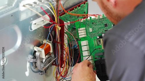 Appliance technician replacing faulty electronic control board inside electric oven. Home appliance repair and component replacement concept