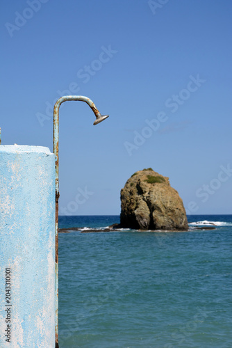 An old abandoned showering facility, with the sea and a rock out of focus in the background in Euboea, Greece
