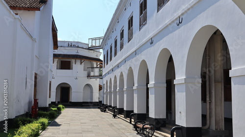 Foto A neat, beautiful lawn featuring a black iron garden bench sits in front of an old white building with numerous arched doorways