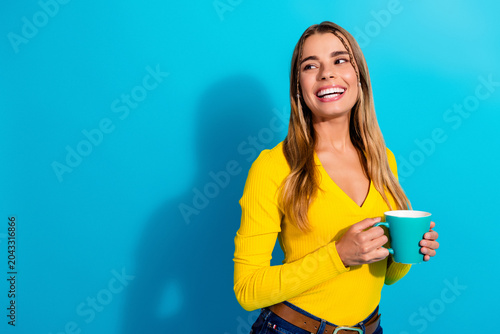 Εκτύπωση καμβά Smiling young woman holding a coffee cup against a bright blue background wearin