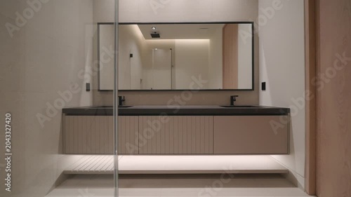 Modern bathroom with long floating vanity and dark countertop, two black faucets create balanced look. Large mirror reflects soft light and clean lines