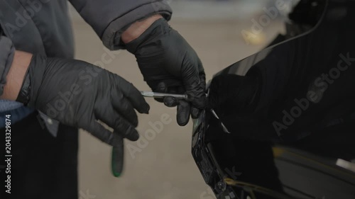 A mechanic wears black nitrile gloves.He works on a black vehicle.The man uses a hand tool.