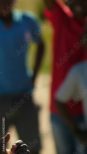 Vertical video: Soccer ball entering left urging teens in tees reaching, catching in sand for play