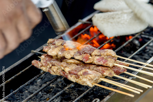 Photos Closeup of raw meat skewers being seared with a kitchen torch on a charcoal gril