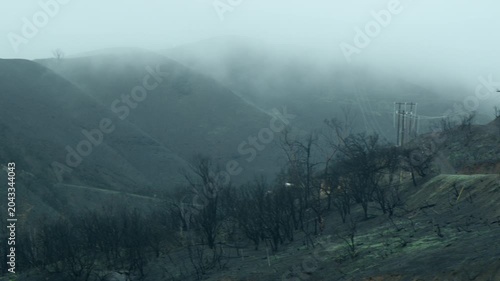 Wildfire damage in hills near Los Angeles shows burnt areas and smoke in the air during a hazy day
