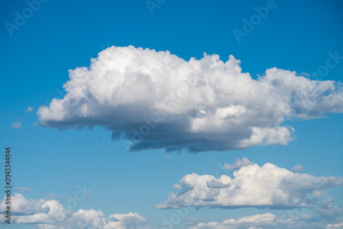 Fotografija A single, large, fluffy white cumulus cloud floats prominently in the center of a clear, bright blue sky, with a few smaller, softer clouds visible near the bottom edge