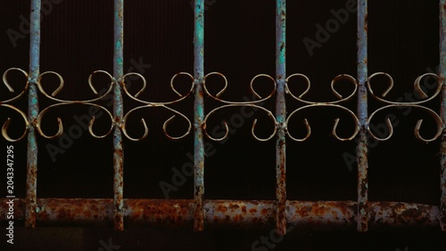 Close-up of a vintage, rusty metal gate with ornate scrollwork against a dark background