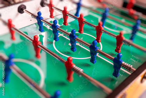 Red and blue plastic players on a green foosball table.