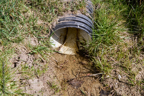 фотографія Outdoor water drainage pipe discharging runoff into grassy soil area during dayl