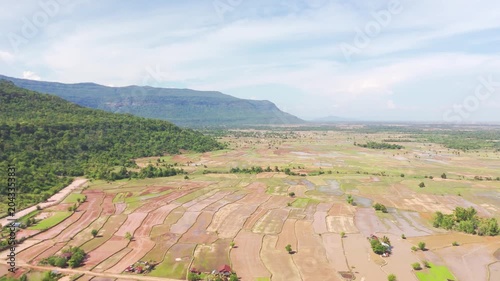 Cinematic drone footage of the tropical forest and agricultural landscape near Khamtay, Attapeu Province, Laos. The aerial view captures the transition from dense jungle on the hillside to the cultiva