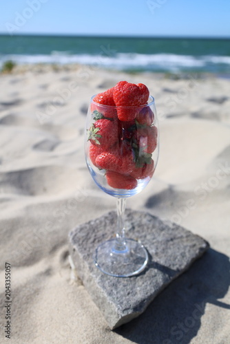Fresh strawberries in a wine glass on a sandy beach