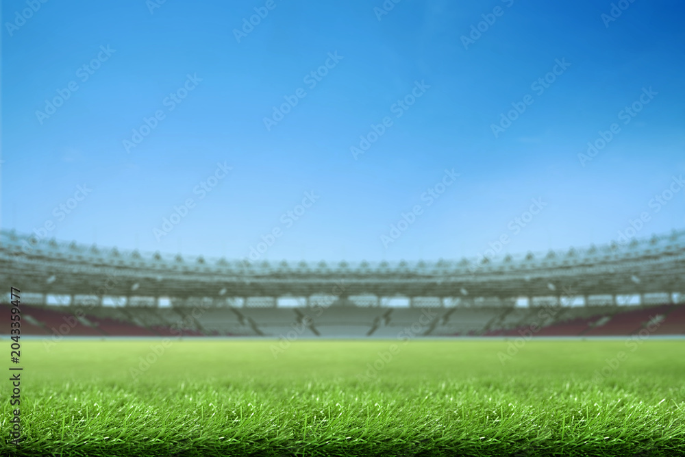 Fototapeta premium Low-angle view of a vibrant green grass field inside a large, empty sports stadium under a clear blue sky